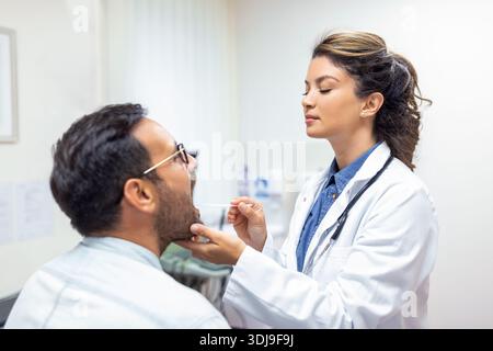 Arzt mit Inspektionsspachtel zur Untersuchung des Rachens des Patienten. HNO-Arzt, der bei einem Mann die Kehle untersucht. Der Patient öffnete seinen Mund zur Kehle Stockfoto