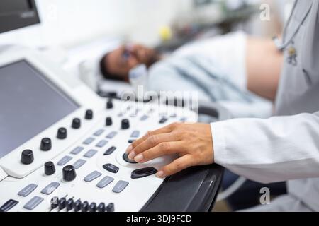Geschickter Sonograf mit Ultraschallgerät bei der Arbeit. Mann, der seinen Arzt zur Ultraschalluntersuchung besucht. Professionelle ärztliche Sonografin im Auftritt Stockfoto