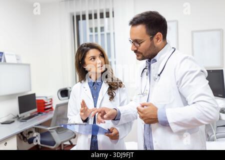 Zuversichtliche Ärzte diskutieren über medizinische Akte. Männliche und weibliche Pflegekräfte tragen Labormäntel. Sie arbeiten im Krankenhaus. Stockfoto