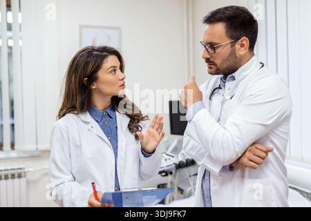 Zuversichtliche Ärzte diskutieren über medizinische Akte. Männliche und weibliche Pflegekräfte tragen Labormäntel. Sie arbeiten im Krankenhaus. Stockfoto