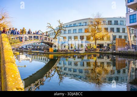 PLONDON, 2. MÄRZ 2025: Eople sammeln sich auf der Iron Footbridge über den Regents Canal in Camden, London. Der Kanal reflektiert an einem sonnigen Tag Gebäude und Bäume in der Nähe. Stockfoto