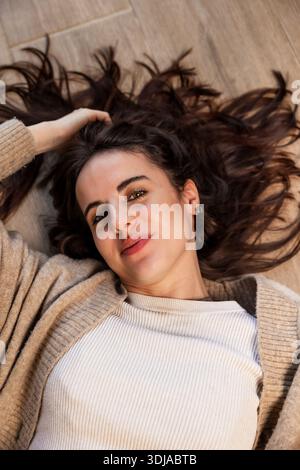 Junge Frau, die sich auf dem Boden mit lockigen Haaren entspannt Stockfoto