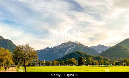 Ein ruhiger Abendblick auf den Höhematte Park in Interlaken, Schweiz. Das Bild zeigt einen leuchtend grünen Rasen, der sich in Richtung des robusten Harder Kulm erstreckt Stockfoto