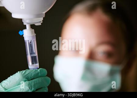 Junge kaukasische Frau, die Maske trägt, die intravenösen Tropfen im Krankenhaus anpasst Stockfoto