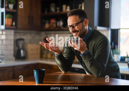 Selbstbewusster, lächelnder Geschäftsmann mit Smartphone im Heimbüro. Überprüfen neuer E-Mails, Videoanrufe Stockfoto
