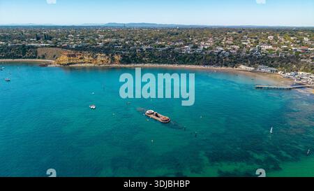 Blick aus der Vogelperspektive auf das historische HMVS Cerberus Schiffswrack in Blackrock Bay, umgeben von Schwimmern, Booten und einem belebten Strand an einem sonnigen Tag. Stockfoto