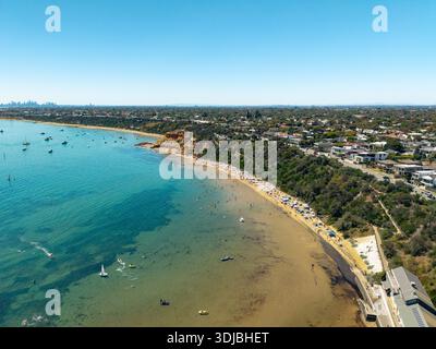Aus der Vogelperspektive fängt Black Rock Beach in Melbourne ein, voller Badegäste und Boote, flankiert von Klippen und Vorstadthäusern. Stockfoto