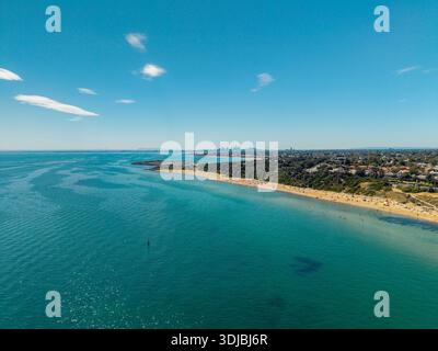 Blick aus der Vogelperspektive auf Black Rock Beach in Melbourne, Australien, an einem sonnigen Tag mit Schwimmern, Sonnenanbetern und der entfernten Skyline der Stadt. Stockfoto