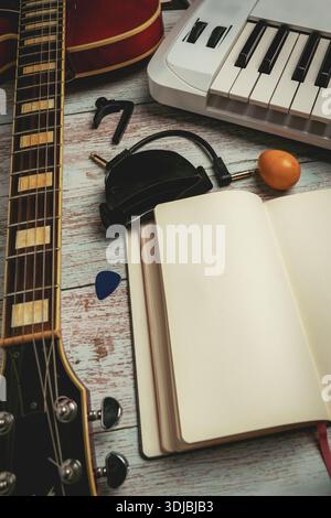Flache Lage des Arbeitsplatzes für die Aufnahme zu Hause mit Gitarre, Tastatur, Mikrofon und leerem Notizbuch auf hölzernem Hintergrund. Musikproduktion und Songwrit Stockfoto