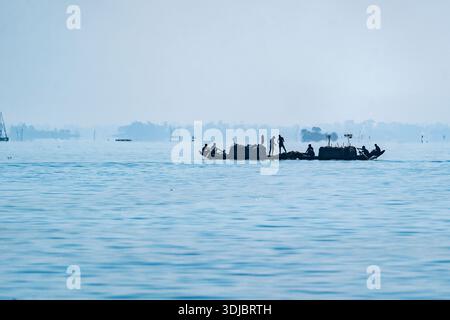 Ruhige Silhouette eines Bootes auf dem Wasser. Fischer werfen Netze auf einem ruhigen See mit Bergen im Hintergrund. Kaptai Lake Rangamati Stockfoto