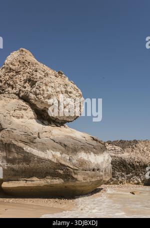 Eine vertikale Nahaufnahme großer, verwitterter Felsformationen an einem Sandstrand in Oman. Die Felsen zeigen verschiedene Strukturen und Farbtöne in Braun und Beig Stockfoto