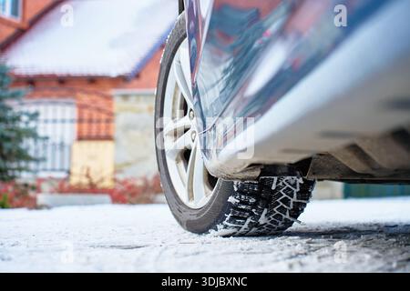 Flacher Blick auf das Autorad mit Winterreifen auf verschneite Straße in der Nähe eines Wohnhauses. Konzept für Winterfahren, Straßensicherheit, kalte Witterungsbedingungen und Stockfoto
