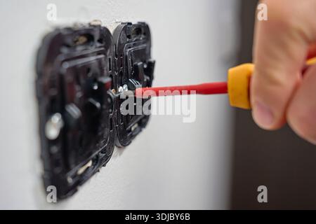 Verwenden Sie einen Schraubendreher, um den elektrischen Wandschaltermechanismus in der weißen Wand zu installieren. Konzept der elektrischen Installation und Reparatur Stockfoto