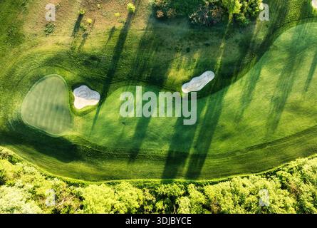 Blick aus der Vogelperspektive auf den Sonnenuntergang über dem Golfplatz mit frühlingshaften Bäumen und Seen Stockfoto