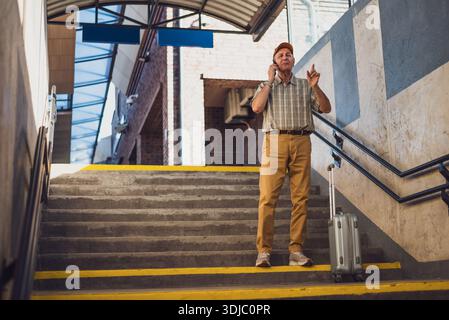 Der Senior Mann steht am Bahnhof und spricht mit dem Handy. Senioren reisen. Stockfoto
