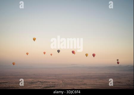 Bunte Ballons verstreut über den Wüstenhimmel bei Sonnenaufgang Stockfoto