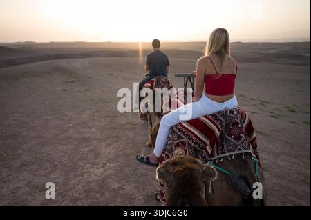 Zwei Leute reiten auf Kamelen bei Sonnenaufgang in der Agafay-Wüste Stockfoto