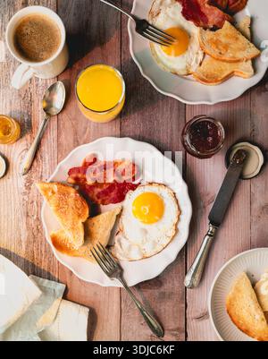 Blick von oben auf die Teller mit Speck, Eiern, Toast und Getränken zum Frühstück. Stockfoto