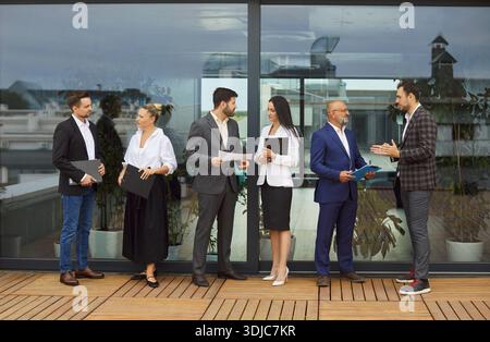 Geschäftsleute, die nebeneinander stehen und wichtige Themen diskutieren, Papierdokumente halten Stockfoto