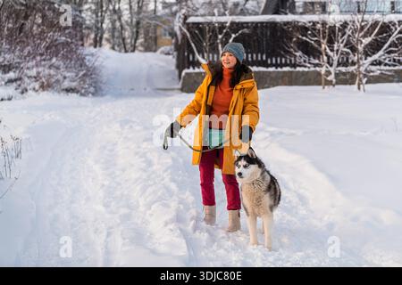 Asiatische Frau läuft im Winter mit ihrem Huskyhund im Schnee. Stockfoto