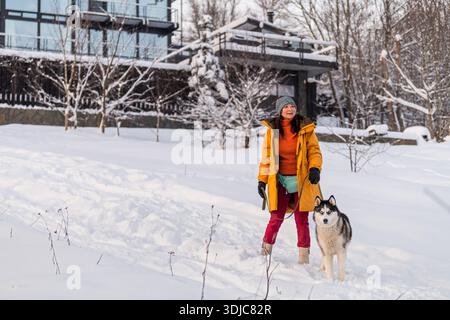Asiatische Frau läuft im Winter mit ihrem Huskyhund im Schnee. Stockfoto