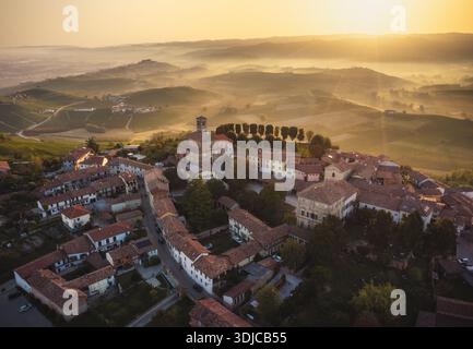 Blick aus der Vogelperspektive auf die Altstadt mit ihren Terrakotta-Dächern, eingebettet in die sanften Hügel und Weinberge, die im goldenen Licht der Morgendämmerung getaucht sind, Verduno, Stockfoto