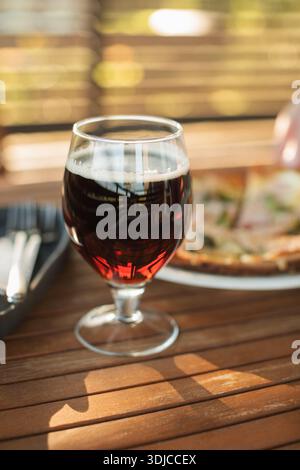 Nahaufnahme eines Glases dunkles Bier und einer Pizza auf einem Gartentisch Stockfoto