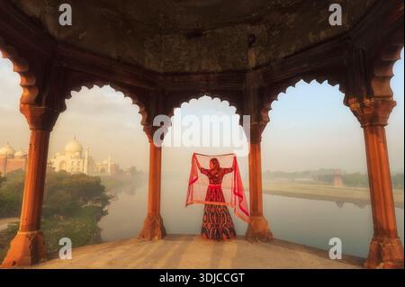 Rückansicht einer jungen Frau am Jamuna-Fluss, die bei Sonnenuntergang ein Tuch über dem Kopf hält, Taj Mahal, Agra, Uttar Pradesh, Indien, Stockfoto