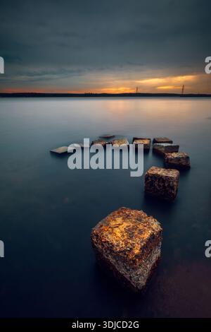 Reihe verwitterter Betonblöcke im Meer bei Sonnenuntergang, Kurischer Golf, Litauen Stockfoto