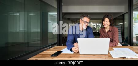 Business-Team aus zwei zufriedenen, vielbeschäftigten Profis, die mit einem Notebook zusammenarbeiten. Stockfoto