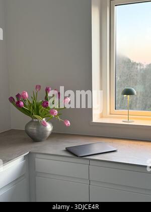 Geschlossener Laptop auf einer Küchentheke neben einer Vase mit rosa Tulpen Stockfoto