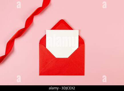 Draufsicht auf roten Umschlag, weiße Karte und rotes Band auf rosa Hintergrund. Valentinstag, Liebe. Glänzender gerollter Stoff, Seide und Satin. Stockfoto