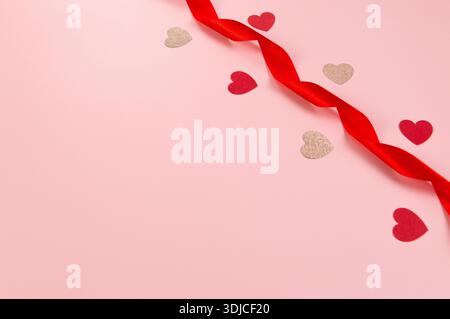 Ansicht von oben auf rotes Band, rote Herzen und rosa Glitzerherzen auf rosa Hintergrund. Valentinstag, Liebe. Glänzender gerollter Stoff, Seide und Satin. Stockfoto