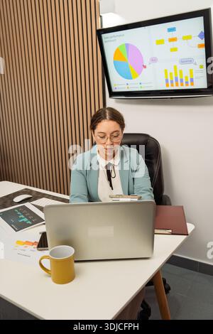 Junge professionelle Frau, die an einem Laptop arbeitet und Daten auf einem Dashboard für die Verkaufsleistung analysiert Stockfoto