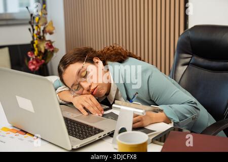Eine junge Frau erlitt Burnout, während sie ihren Kopf auf einem Laptop am Schreibtisch auslegte Stockfoto