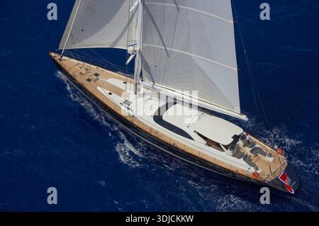 Blick aus der Vogelperspektive auf die luxuriöse Segelyacht Dakota (ex GANESHA) mit weißen Segeln und Holzdeck aus Teakholz, die über den tiefblauen Ozean gleiten Stockfoto