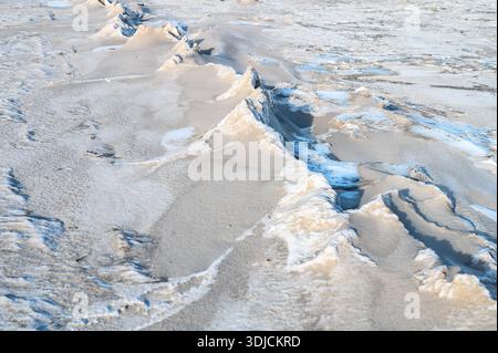 Gefrorene Sanddünen mit blauen Eisformationen am Ostseestrand im Winter. Natürliche Frostmuster schaffen abstrakte Texturen auf schneebedeckten Sandküsten-lan Stockfoto