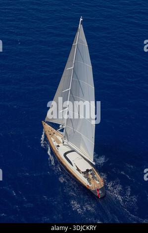 Blick aus der Vogelperspektive auf die luxuriöse Segelyacht Dakota (ex GANESHA) mit weißen Segeln und Holzdeck aus Teakholz, die über den tiefblauen Ozean gleiten Stockfoto