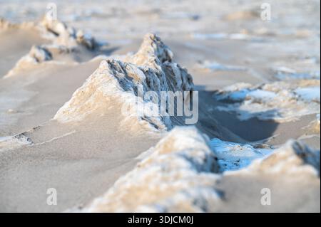 Gefrorene Sanddünen mit blauen Eisformationen am Ostseestrand im Winter. Natürliche Frostmuster schaffen abstrakte Texturen auf schneebedeckten Sandküsten-lan Stockfoto