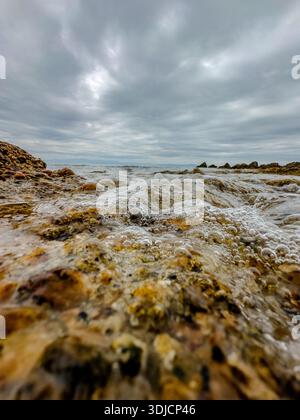 Flacher Blick auf kleine Wellen, die über Kieselsteine und Felsen brechen, an einem Mittelmeerstrand in Afytos, Chalkidiki, Griechenland. Geringe Schärfentiefe, strukturiert Stockfoto