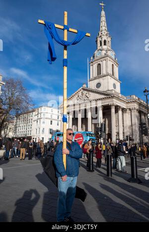 Mann mit einem riesigen Kreuz, das mit blauem Tuch vor blauem Himmel hängt, neben der St. Martin-in-the-Fields Kirche, Trafalgar Square, London, England, Großbritannien Stockfoto