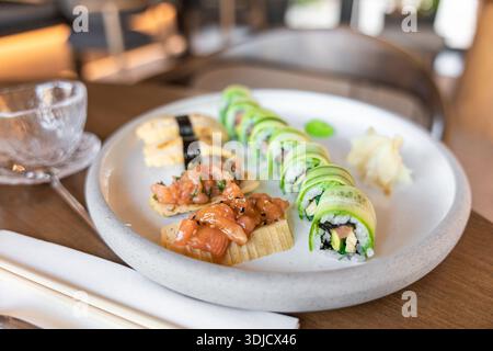 Ein Teller Sushi mit Lachsnigiri und Gurkenrollen. Das Gericht wird mit eingelegtem Ingwer und Wasabi auf einem Holztisch serviert. Stockfoto