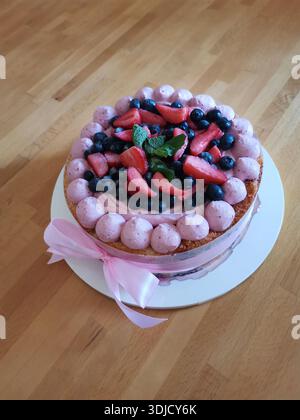 Köstlicher Frischkäse-Mousse-Kuchen mit cremigem Zuckerguss, bedeckt mit frischen Erdbeeren, Heidelbeeren und Minzzweig Stockfoto