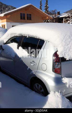 Unter einem gnadenlosen weißen Grabtuch begraben, kämpft ein elegantes rotes Coupé um das Überleben gegen den wilden Winterangriff St. Bad Wiessee, Bayern. Stockfoto