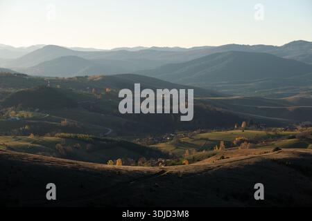 Blick auf die hügelige ländliche Landschaft mit Weiden, die früh am Morgen beleuchtet werden, und Berge im Dunst in der Ferne am Berg Zlatibor, besuchen Sie Serbien Countrys Stockfoto