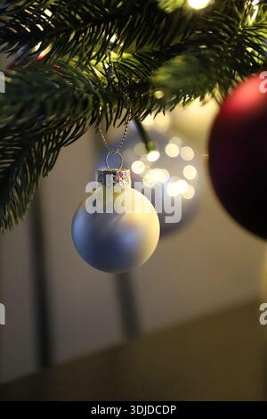 Nahaufnahme einer silbernen Weihnachtskugel, die an einem Tannenzweig hängt, mit weichen warmen Bokeh-Lichtern im Hintergrund. Festliche Dekoration für Winterferien. Stockfoto