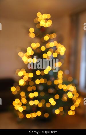 Verschwommenes Nahfoto eines verzierten Weihnachtsbaums mit vielen warmen Lichtern, Hintergrund. Stockfoto