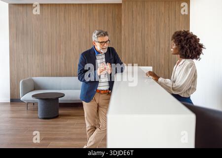 Männliche Profis checken ein und besprechen die Details der Zimmerreservierung mit der Rezeption in der Hotellobby Stockfoto