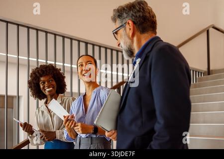 Geschäftsmann, der Dokumente hält, um Ideen mit weiblichen Kollegen zu diskutieren, während er im Büro Treppen betritt Stockfoto