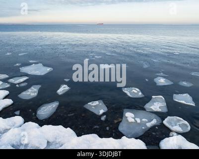 Luftperspektive schwimmender Eisschollen in der kalten Ostsee mit einem fernen Frachtschiff unter Winterhimmel. Stockfoto